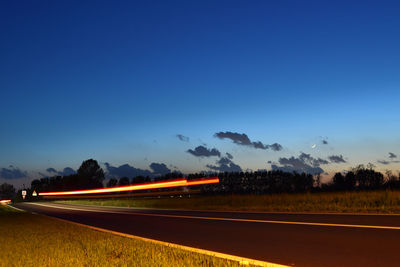 Road amidst field against clear blue sky