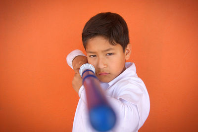Portrait of boy holding toy sword against orange background