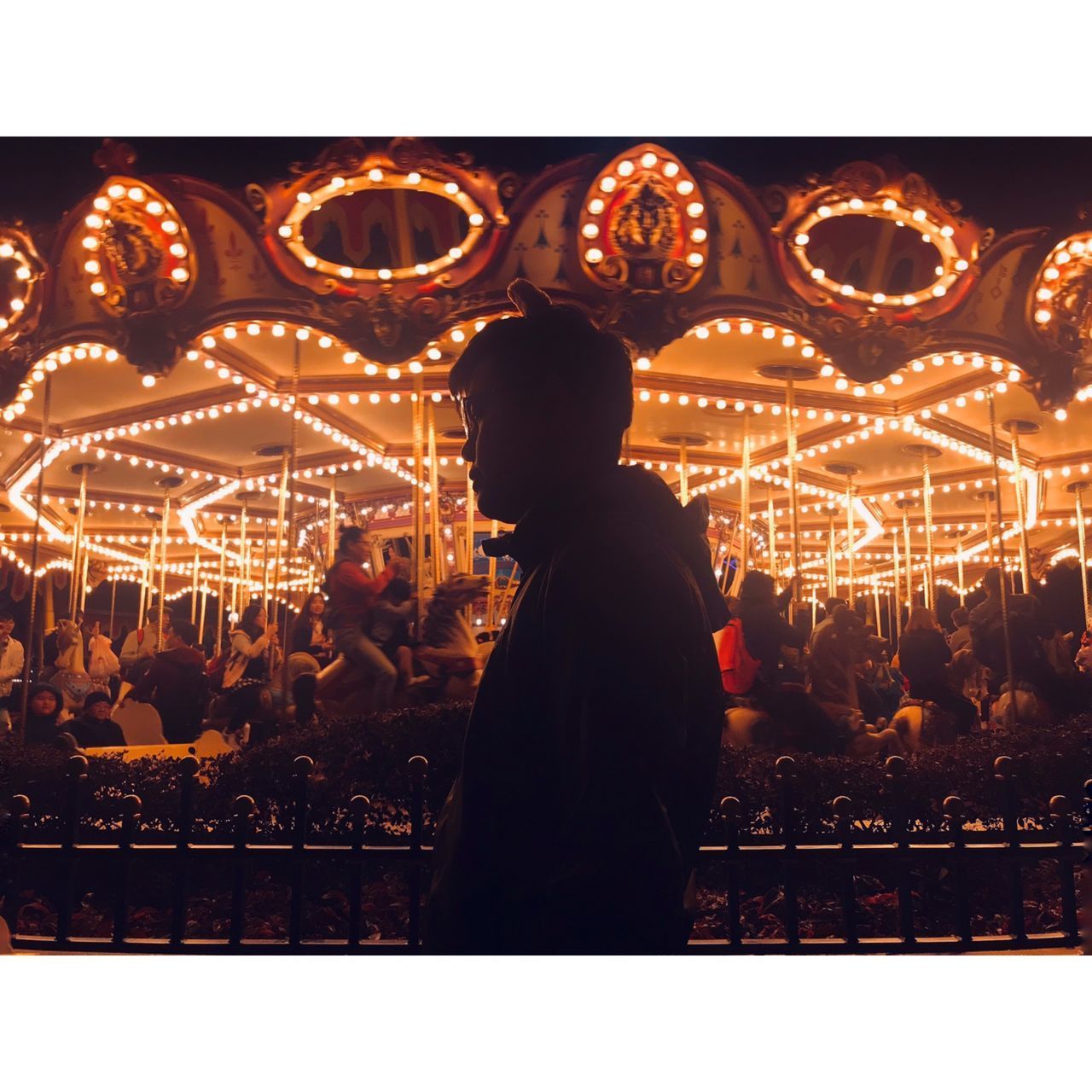 REAR VIEW OF PEOPLE AT ILLUMINATED AMUSEMENT PARK