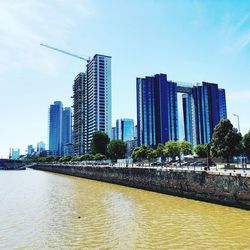 Modern buildings by river against sky in city