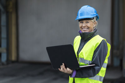 Portrait of happy mature female worker using laptop at factory