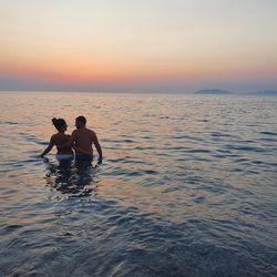 People in sea against sky during sunset