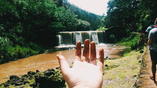 Close-up of person showing dirty hand by waterfall
