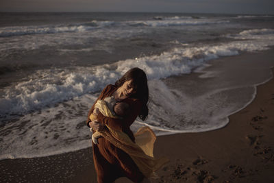 Smiling woman walking with newborn baby boy at beach