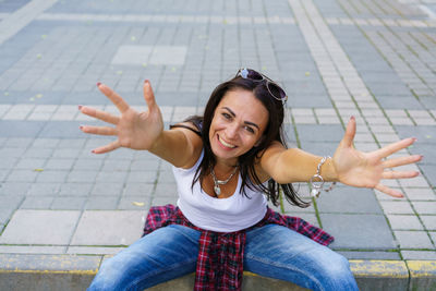 Happy girl in white t-shirt, blue jeans and white sneakers sits on sidewalk