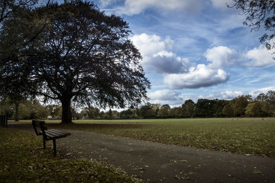 Empty bench on field by trees against sky