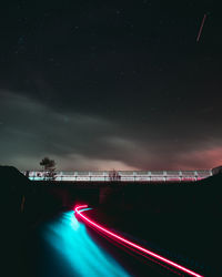 Light trails on illuminated bridge against sky at night