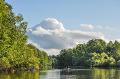 Person rowing boat on lake against sky