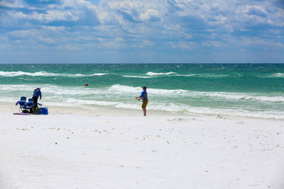 People enjoying at beach against clear blue sky