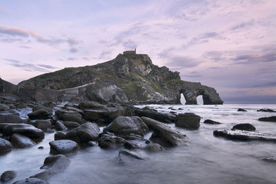 Rocks on sea shore against sky during sunset