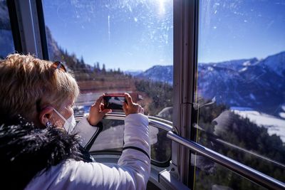 Women with mouth and nose protection is taking photos with her cellphone in the cable car