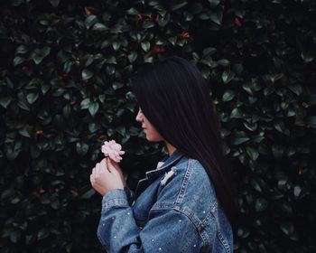 Side view of woman holding flower standing by plants