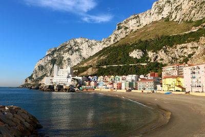 Road by sea and buildings against sky in city