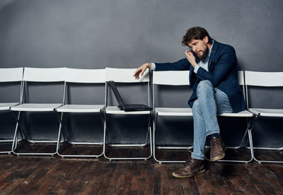 Man using laptop while sitting on chair against wall