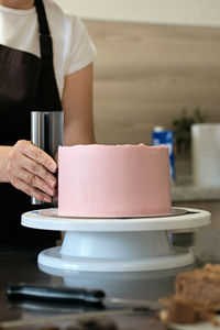 Woman pastry chef making chocolate cake with pink cream, close-up. cake making process