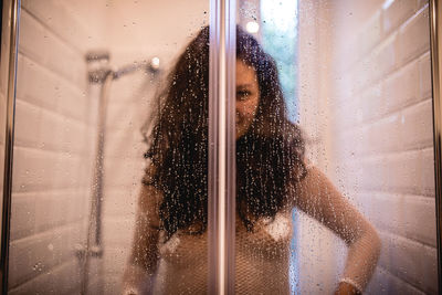 Woman seen through wet glass window in bathroom