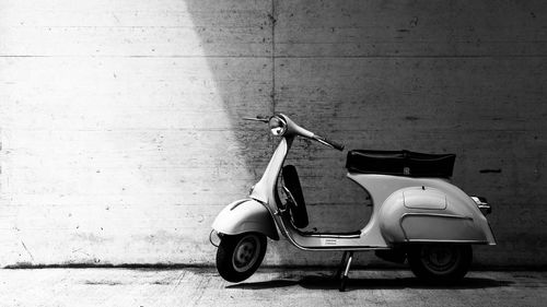 Side view of motor scooter parked on footpath against wall