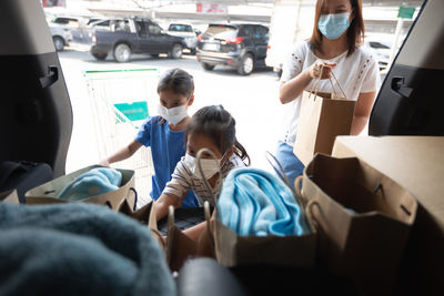 Mother and daughter wearing mask putting grocery in car