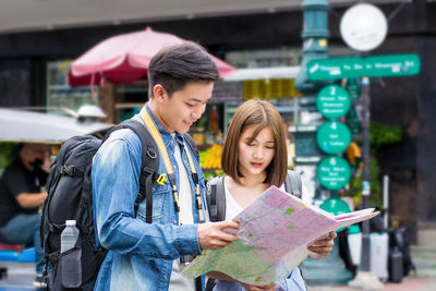 Smiling couple with map standing on street in city