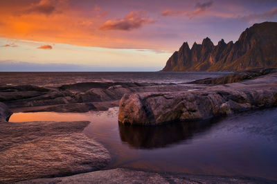 Rocks in sea against sky during sunset