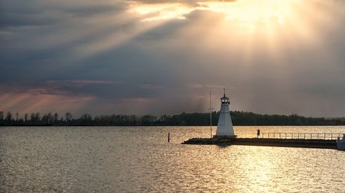 Lighthouse by lake against sky during sunset