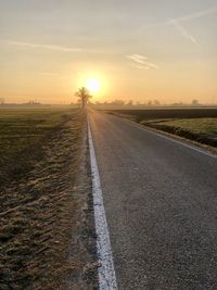 Road amidst field against sky during sunset