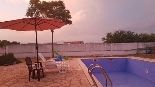 Chairs and table by swimming pool against sky