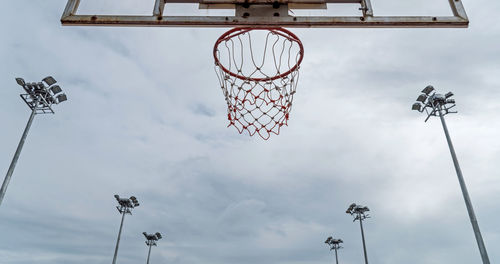 Low angle view of basketball hoop and floodlights against cloudy sky