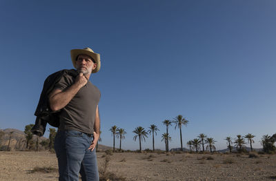 Adult man in cowboy hat on tabernas desert with palm trees against blue sky. almeria, spain