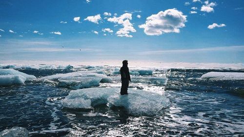 Silhouette man standing on rock by sea against sky