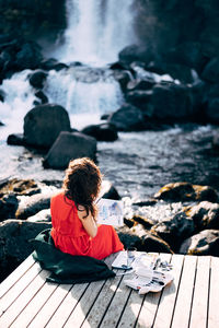 Rear view of girl sitting on rock by water