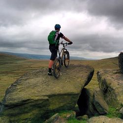 Rear view of man standing on mountain against cloudy sky