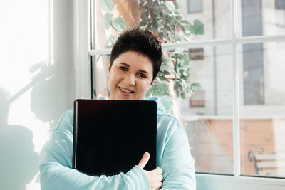 Portrait of smiling woman sitting on window at home