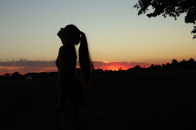 Side view of silhouette woman with ponytail standing against sky during sunset