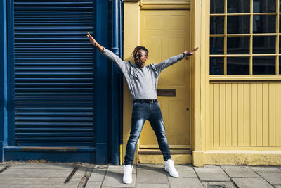 Young man with arms outstretched leaning on yellow house entrance door