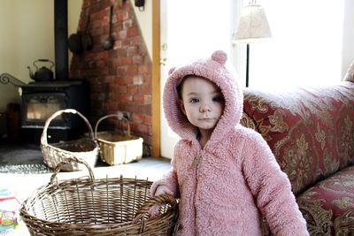 Portrait of cute baby girl by basket and sofa at home