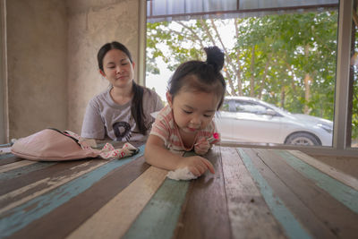 Portrait of mother and girl sitting on window