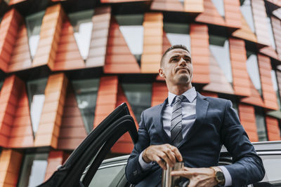 Low angle view of businessman standing near car in front of building