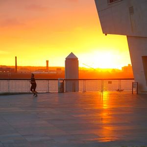 Silhouette man by building against sky during sunset