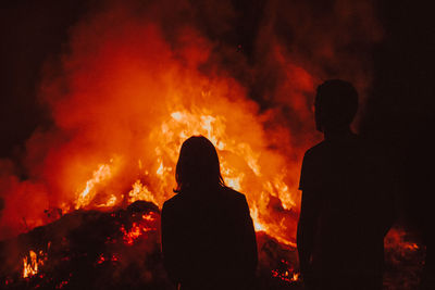 Silhouette man and woman sitting by bonfire at night