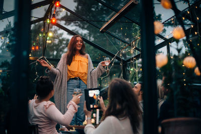 Young woman standing while singing for friends in glass cabin