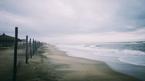 Fence at beach against sky