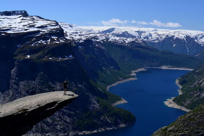 High angle view of person standing at trolltunga against snowcapped mountains