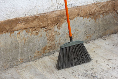 A large street cleaning broom stands against a concrete wall on the asphalt.