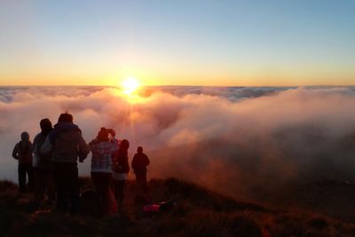 Rear view of people on landscape against sky during sunset