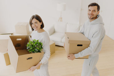 Portrait of couple carrying boxes in new house