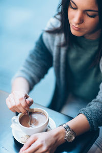 Young woman holding coffee cup at sidewalk cafe in city