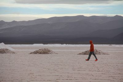 Rear view of man walking on shore against mountains