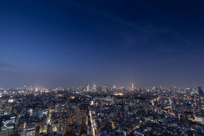 High angle view of city lit up against blue sky