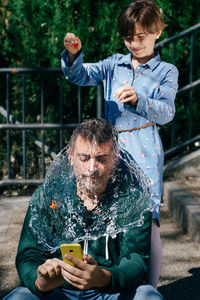 Girl spilling water on father head outdoors